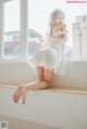 A woman in a white dress sitting on a window sill.