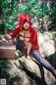 A woman in a red hooded outfit sitting on a rock with a basket.