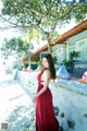 A woman in a red dress standing next to a tree.