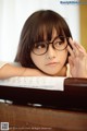 A young woman wearing glasses sitting at a piano.