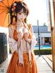 A woman in an orange kimono holding an umbrella.