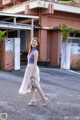 A woman in a purple top and a white skirt is walking down the street.